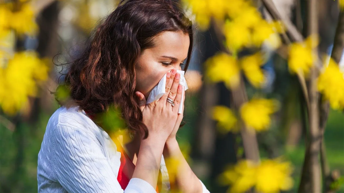 a woman with allergies blowing her nose