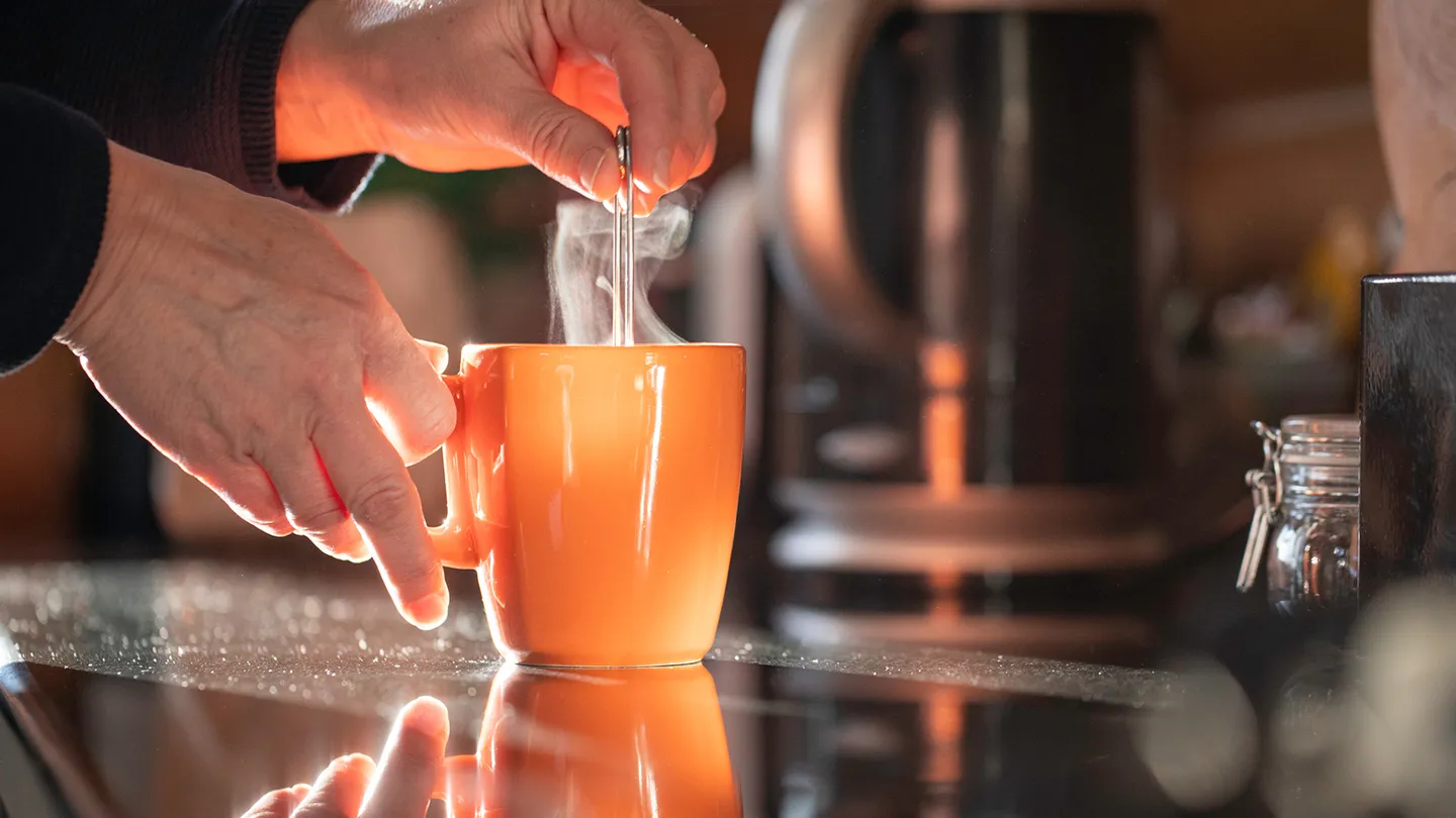 hands stirring orange mug of tea, sunshine and steam 