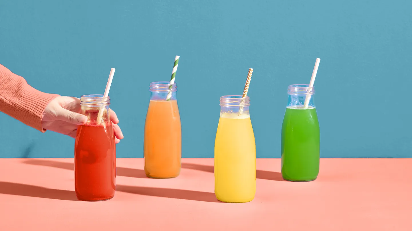 hand reaching for a colorful red juice; pressed fruits; juice cleanse