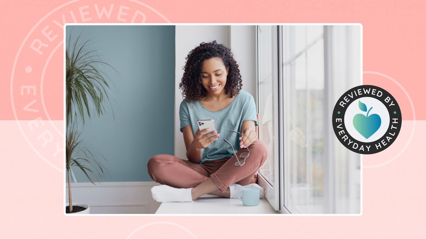 young mixed race woman looking at her phone sitting in a window at home