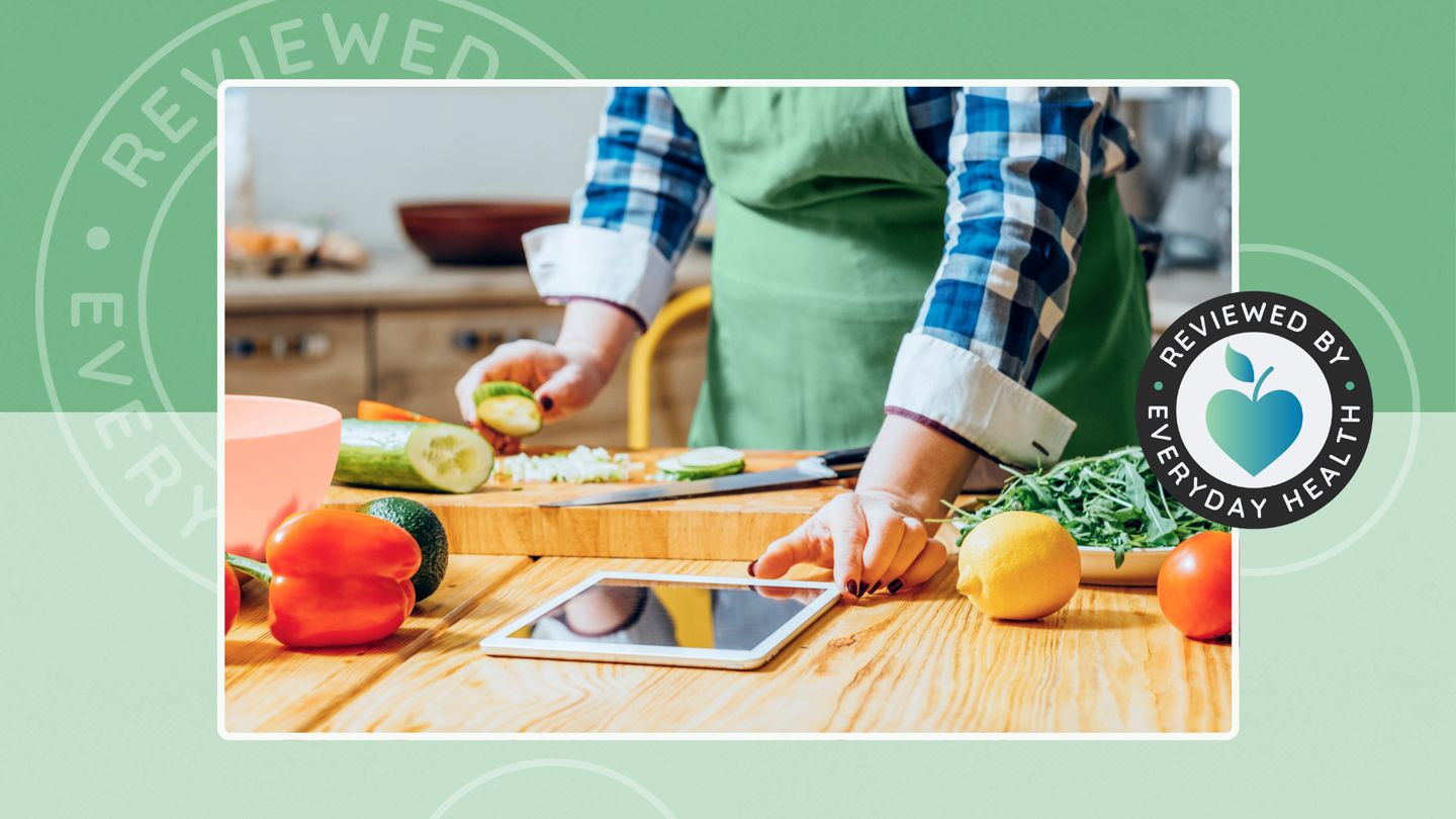 Person using tablet while preparing vegetables on cutting board