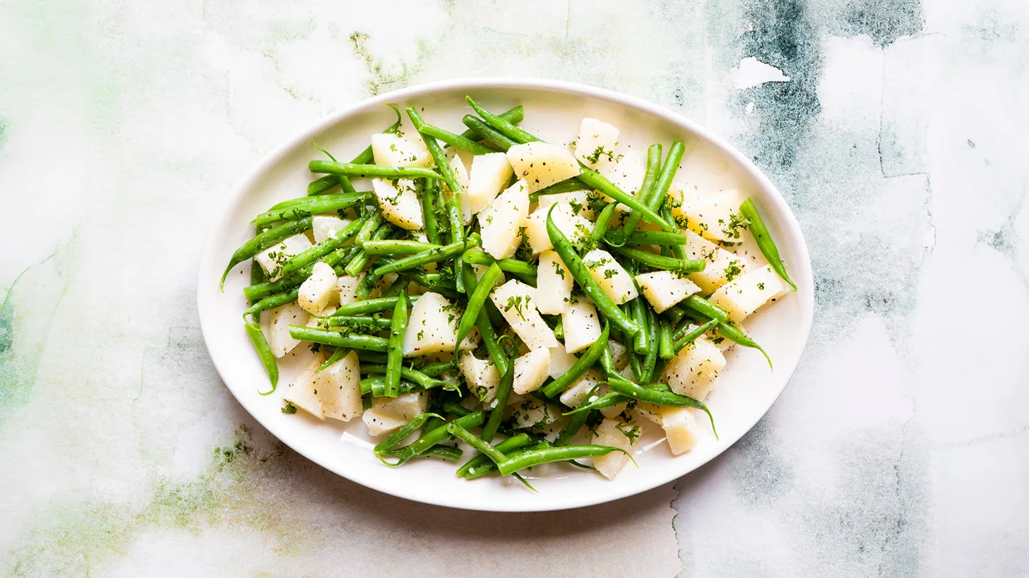cooked Potato and green bean salad on white plate on blue and green and beige kitchen marble countertop