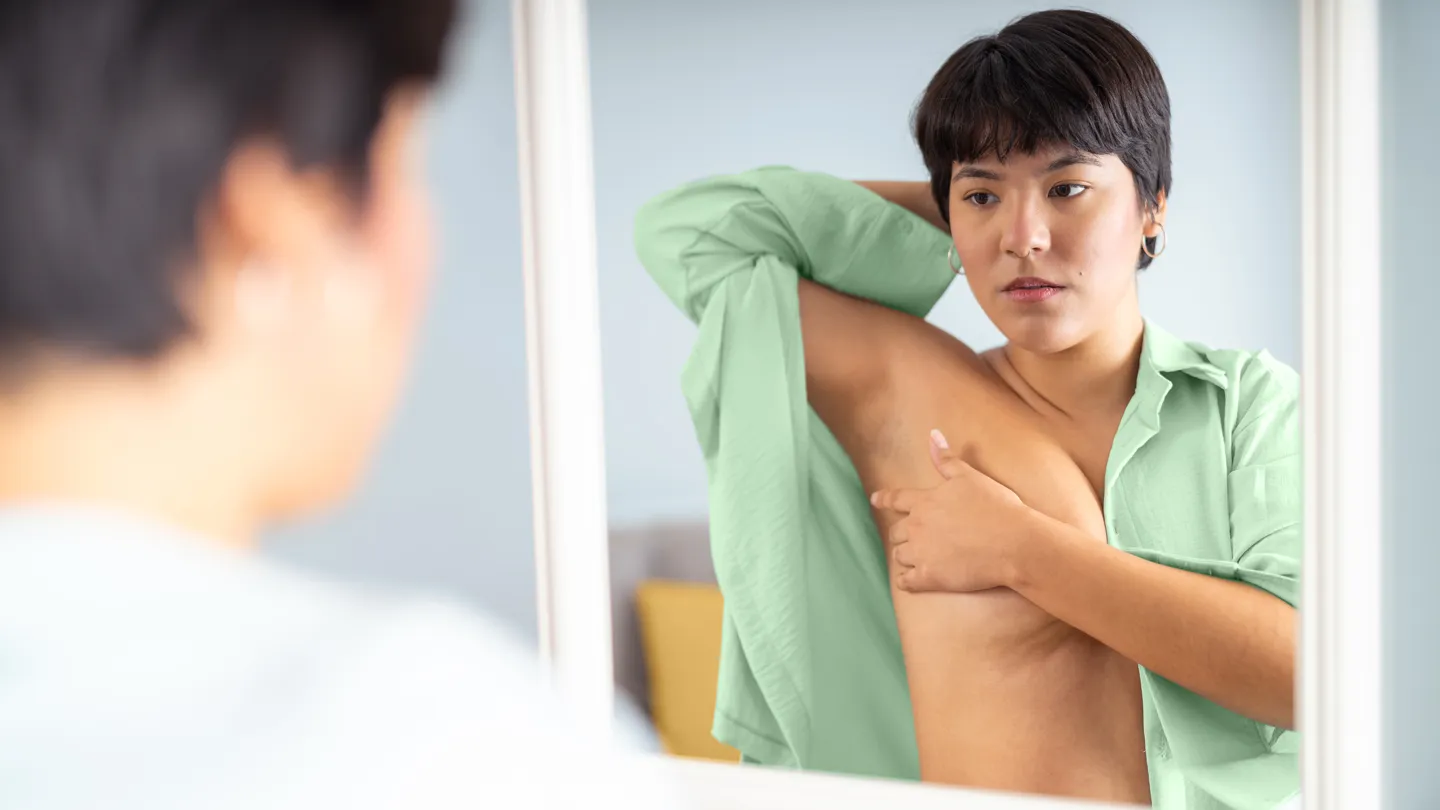 concerned woman doing a self breast exam in the mirror