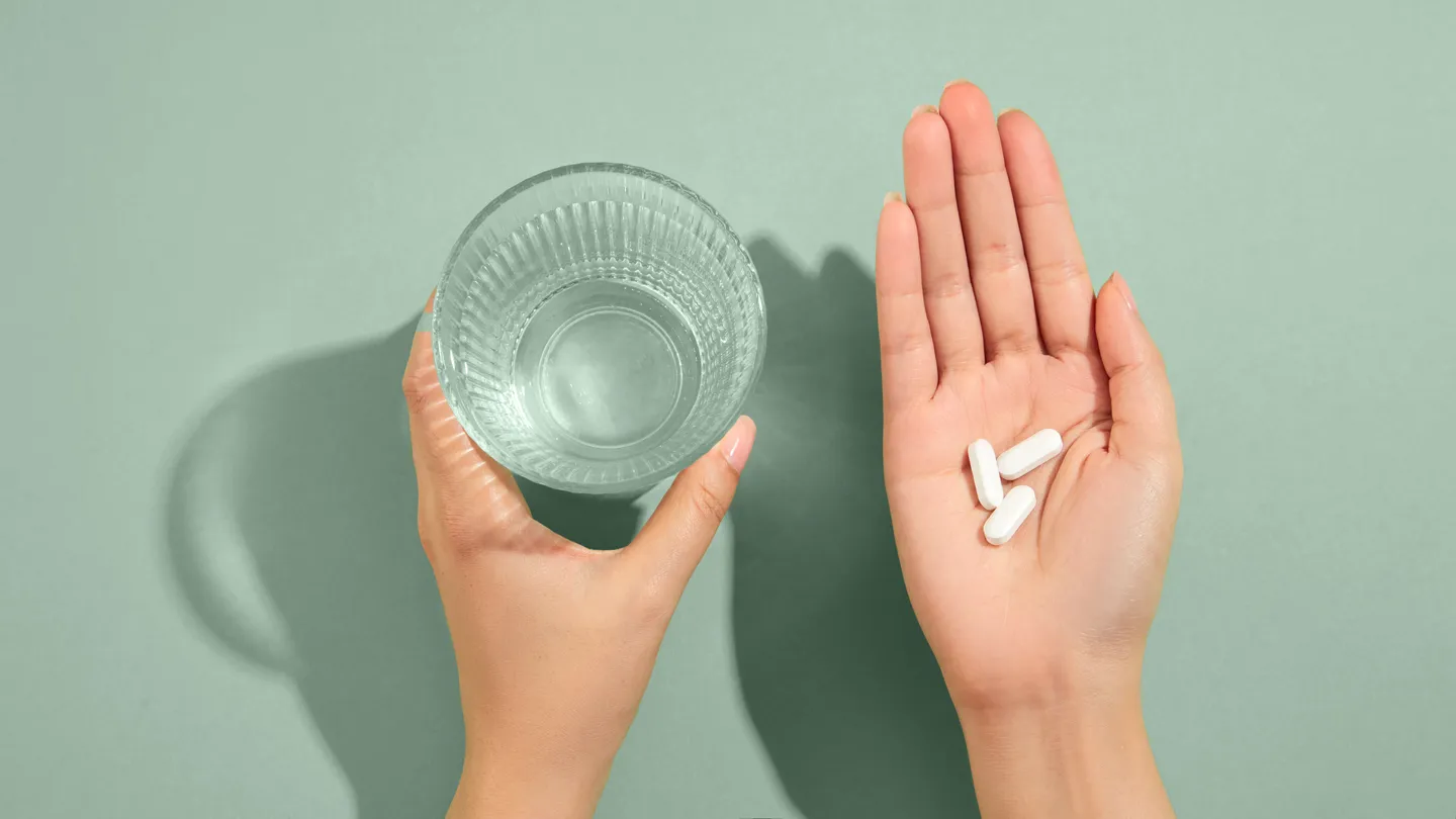 Overhead view of hands holding a glass of water and the other with three oral pills