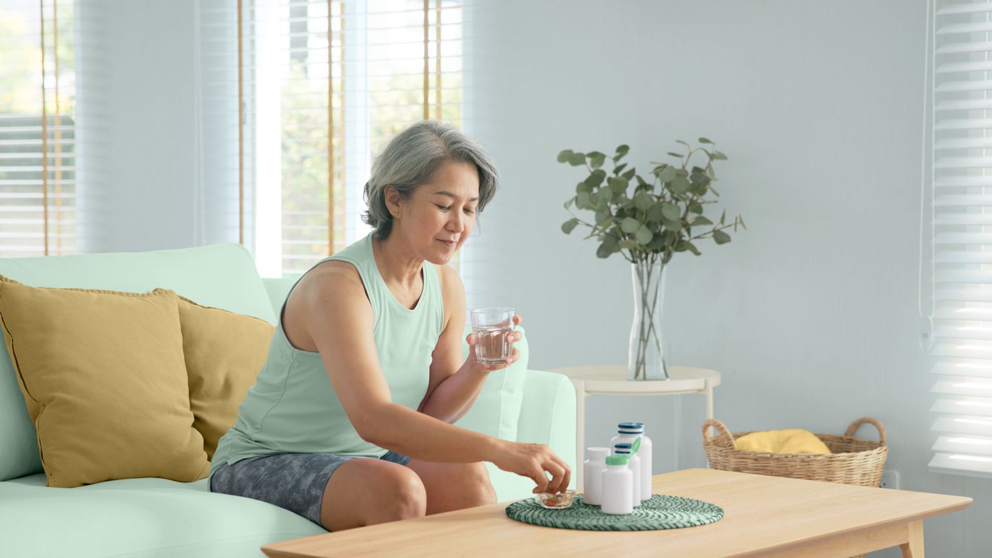 Mature woman taking supplements sitting on her couch at home