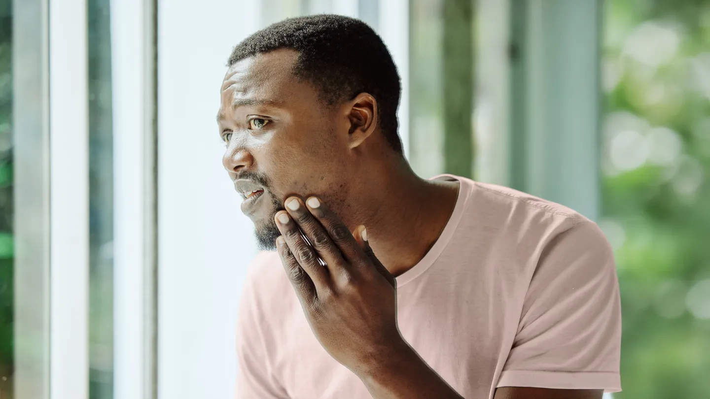 Black man looking at skin on his cheek concerned in the mirror