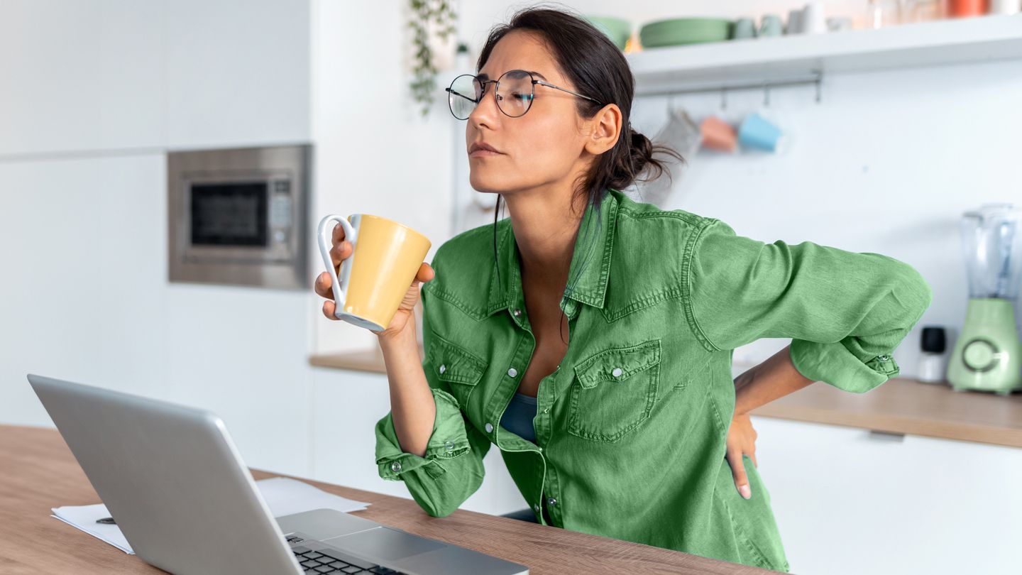 woman with back pain looking uncomfortable while working from home on laptop