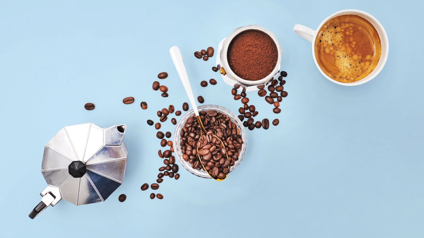Coffee maker, beans, grounds and a cup of coffee against blue background