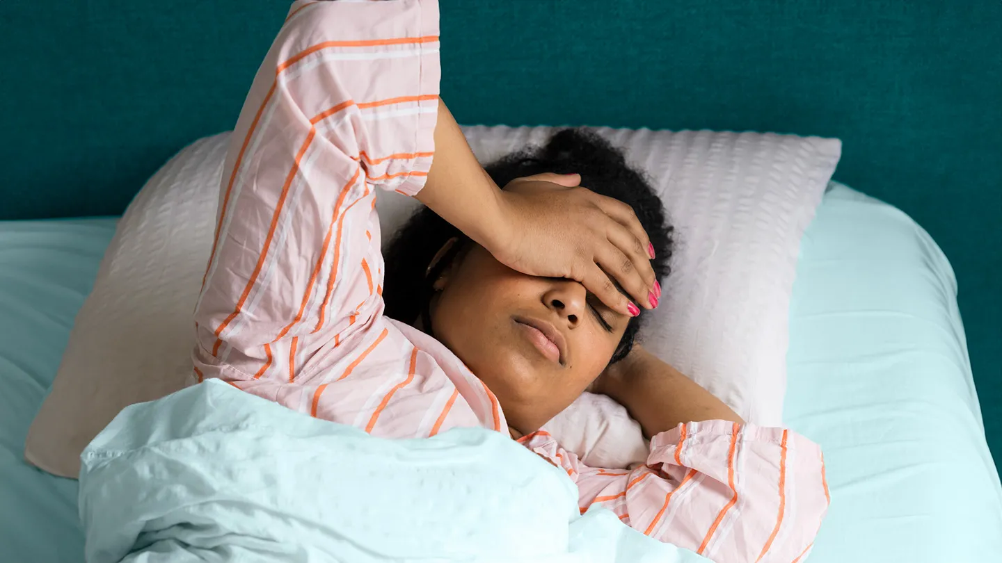 tired looking woman in bed hand on forehead looking exhausted and sleep deprived