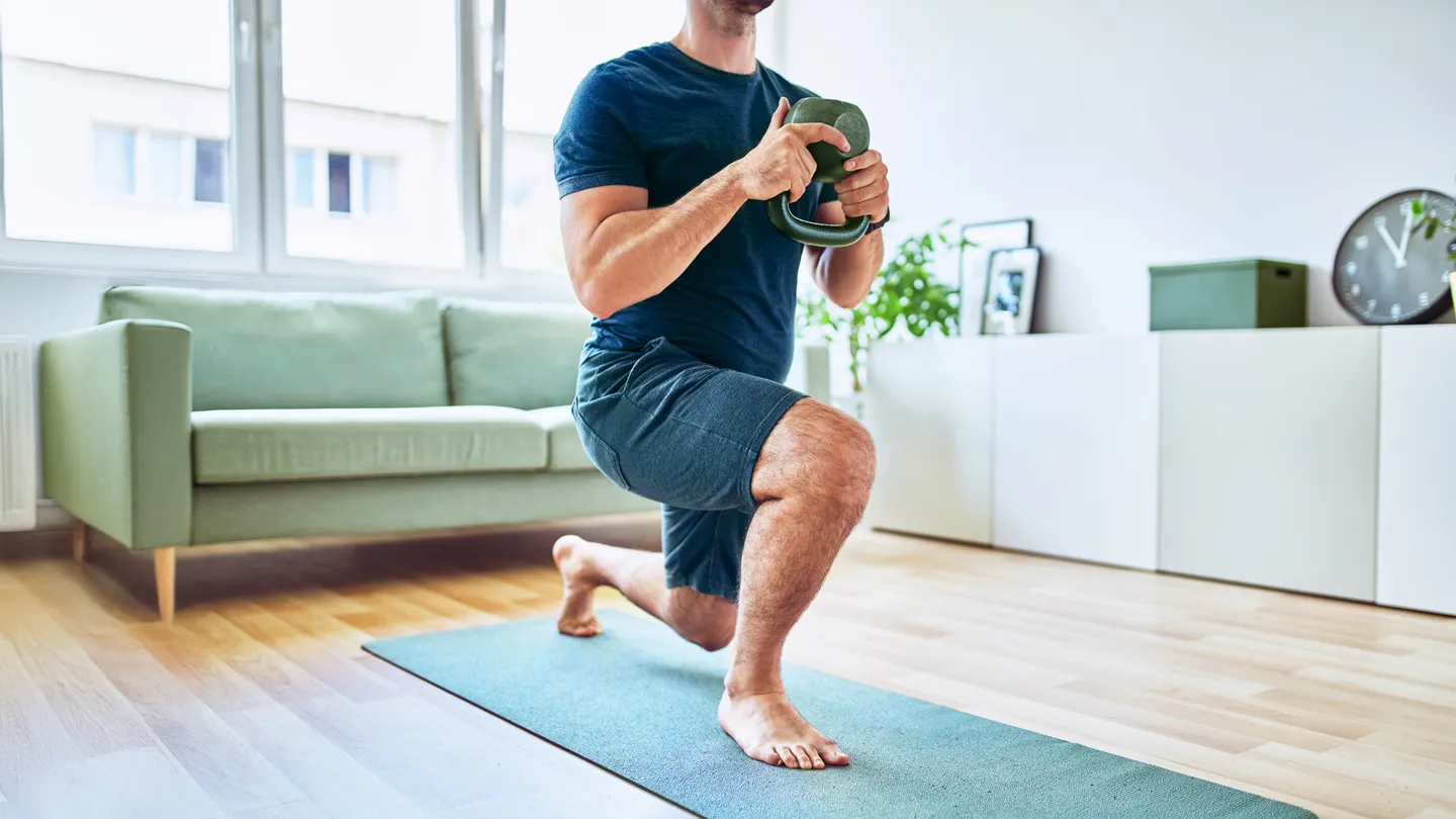 Muscular young man exercising in his living room lifting a kettlebell