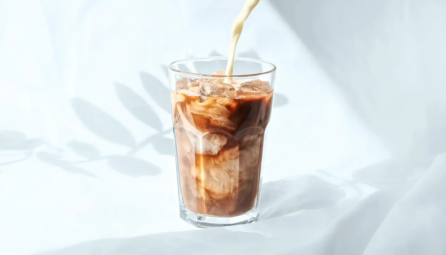 creamer being poured into glass of ice coffee