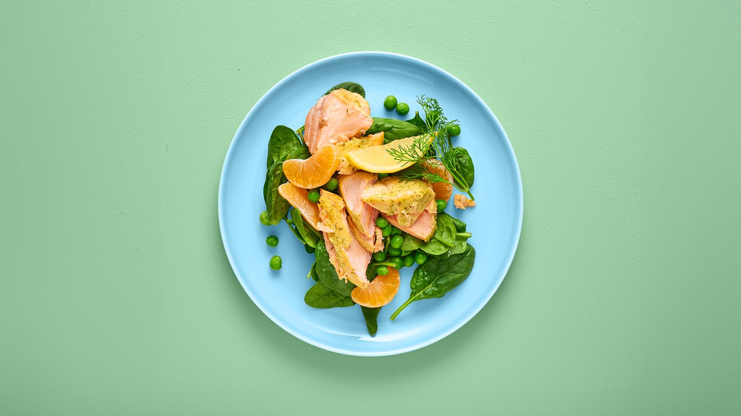 Delicious salad of salmon and spinach oranges peas and artichokes on a blue plate on a green background