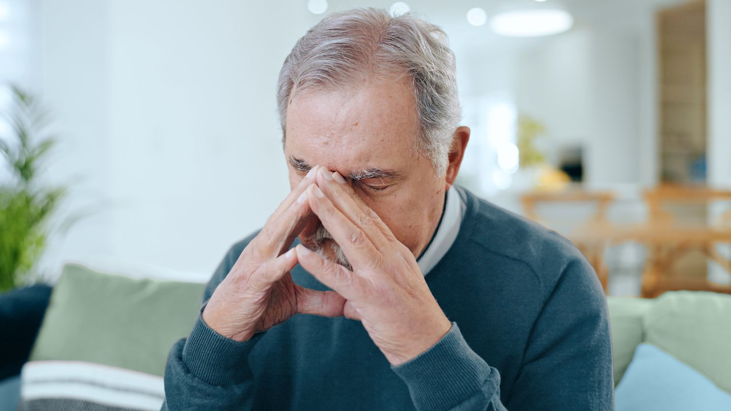 senior man tired head in hands on the couch