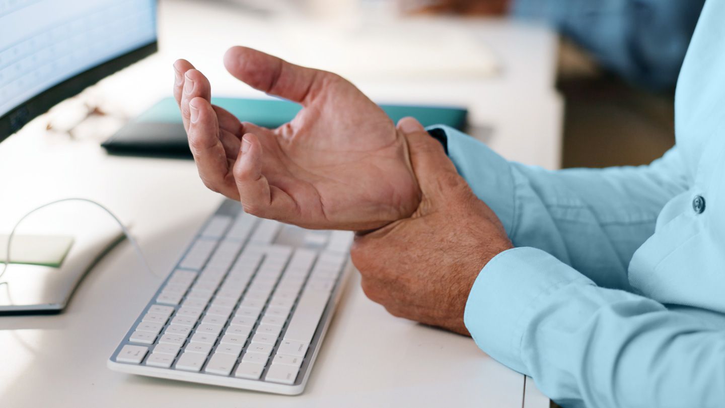 mature business man painfully holding his wrist because of carpal tunnel at his desk