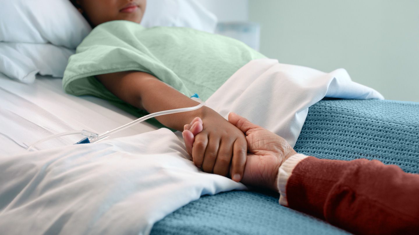 father holding his child's hand in hospital bed