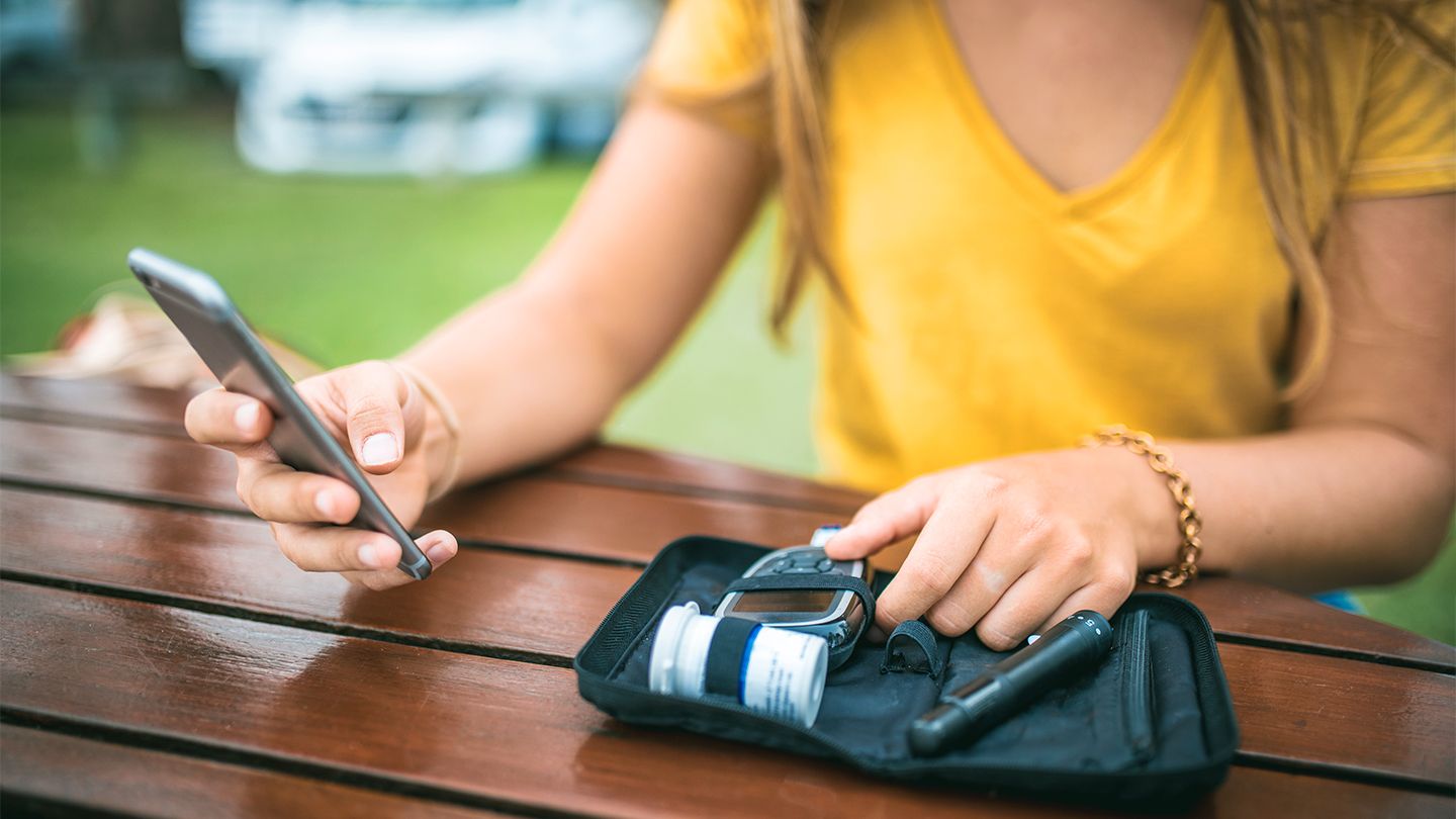 Young woman measuring blood sugar level and using mobile phone type 1 diabetes