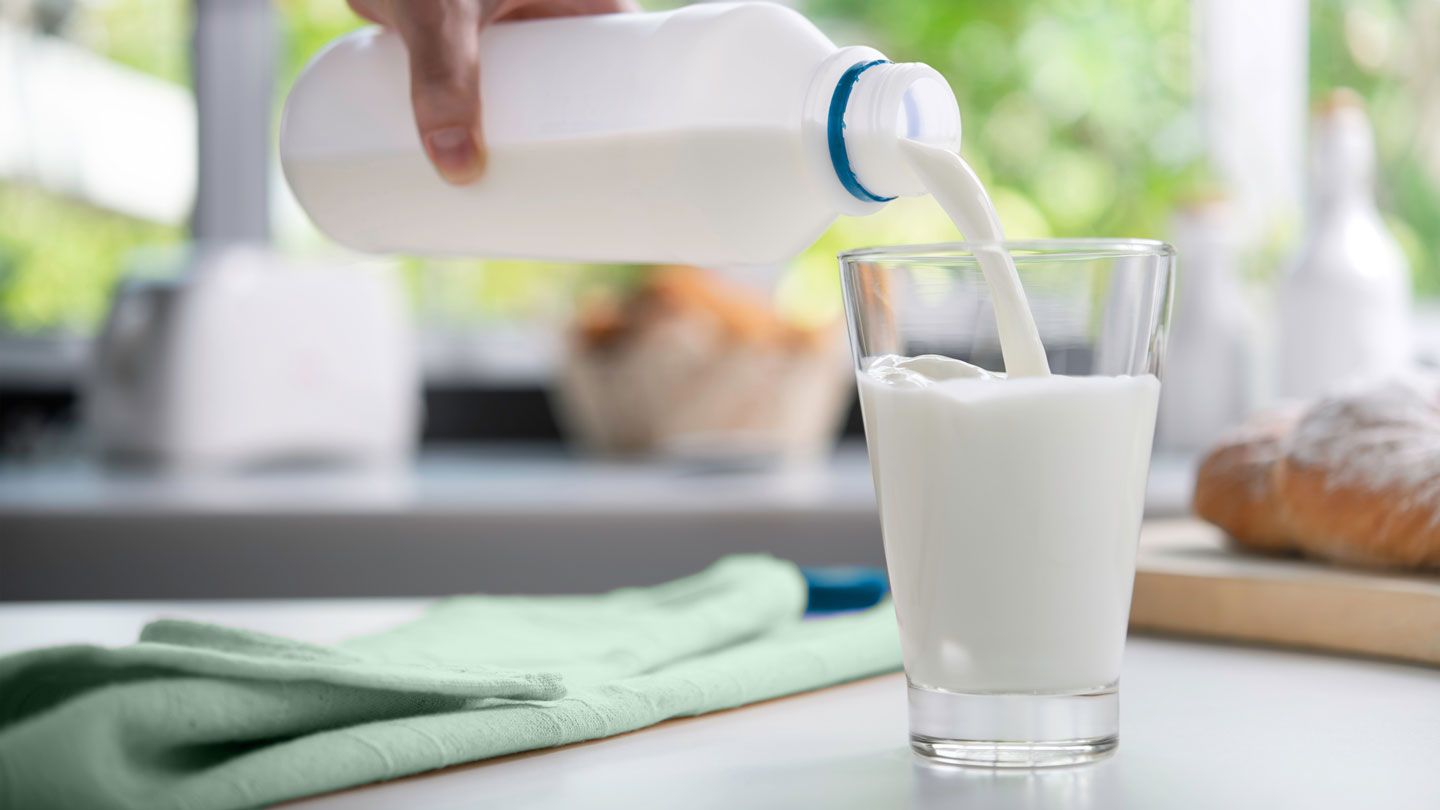 Hand pouring milk into a glass in a kitchen