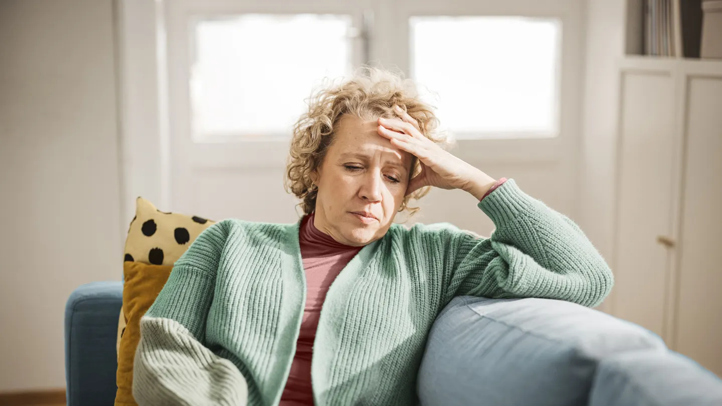Older woman holding head while sitting on a couch