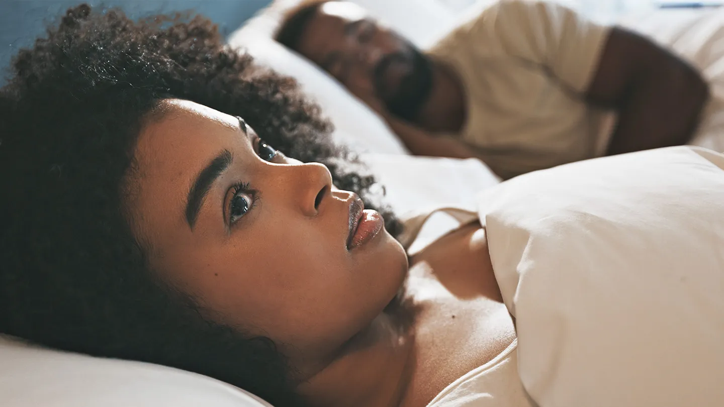 woman having sleep troubles and man sleeping in bed
