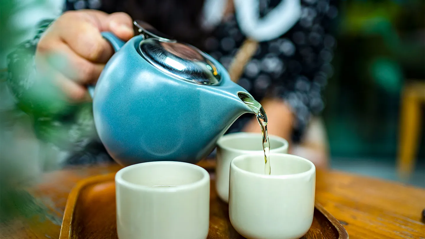 blue teapot pouring tea into three cups