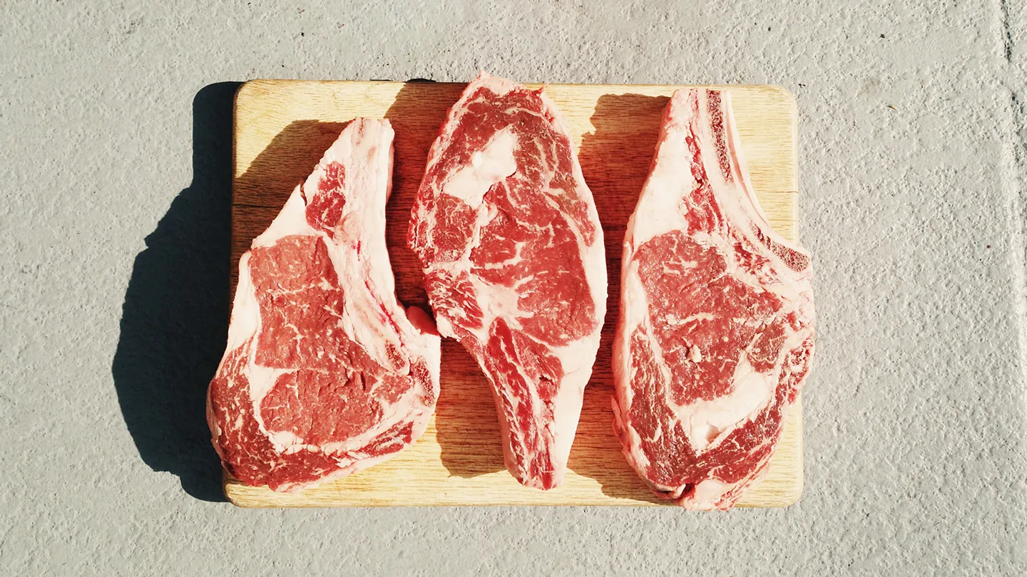 raw steaks on cutting board in the sun on concrete