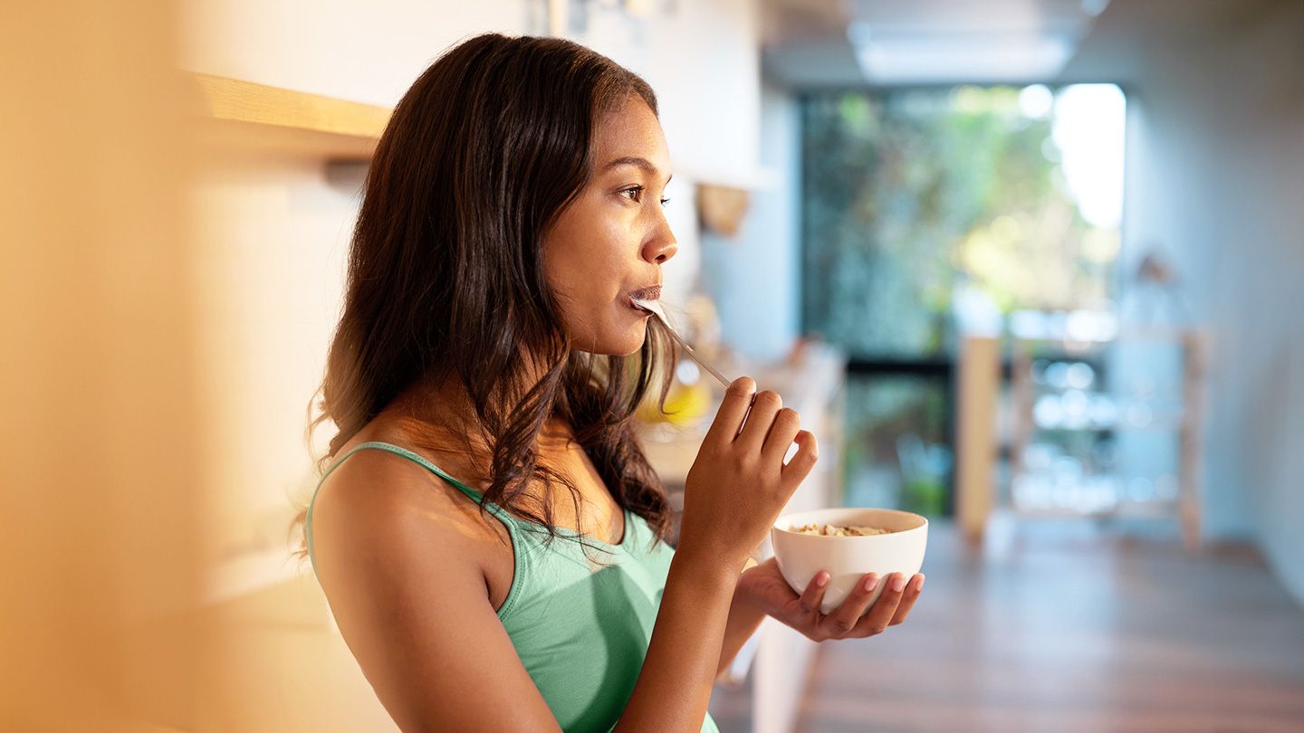 young woman taking a moment to enjoy a small bowl of yogurt and fortified breakfast cereals savoring her small meal in kitchen setting with warm light