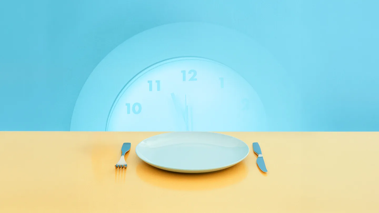 empty plate and silverware on yellow surface with fading wall clock behind with late time of almost midnight 12 am
