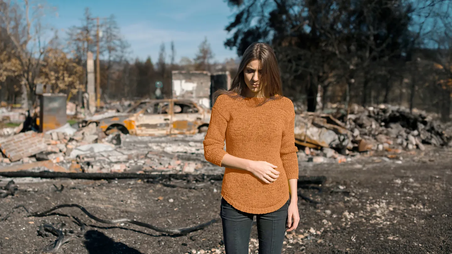 devasted woman standing in front of destroyed property by fire