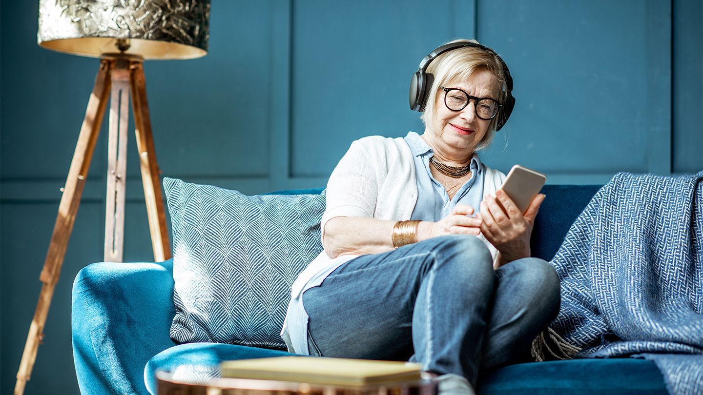woman on blue couch with headphones on listening to phone