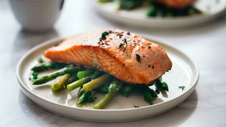 Salmon fillet on top of asparagus on white plate sitting on white marble table top