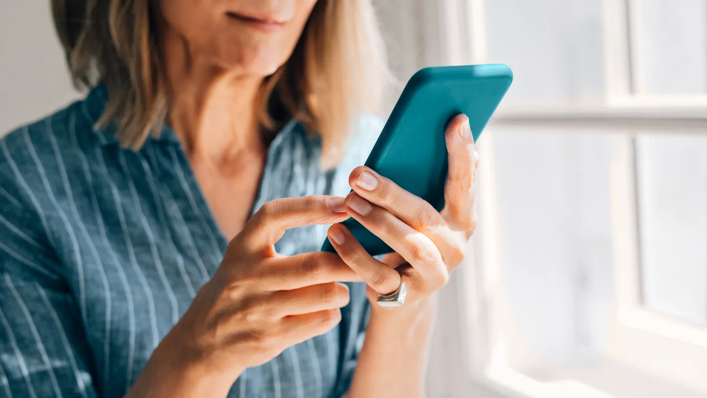mature woman looking at smart phone at home in front of sunny window