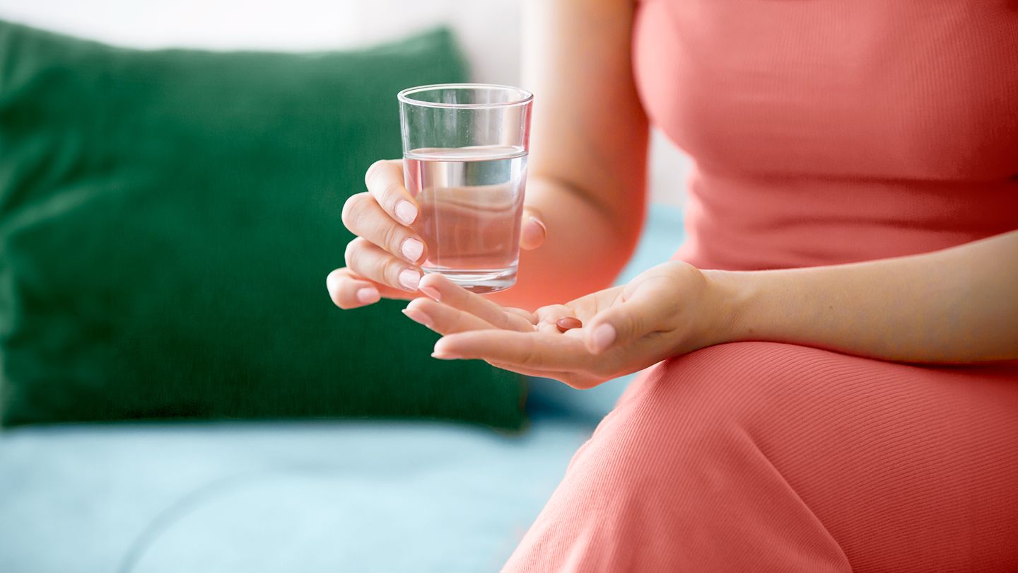 woman in athletic wear holding over the counter nsaid painkiller pill medicine and glass of water