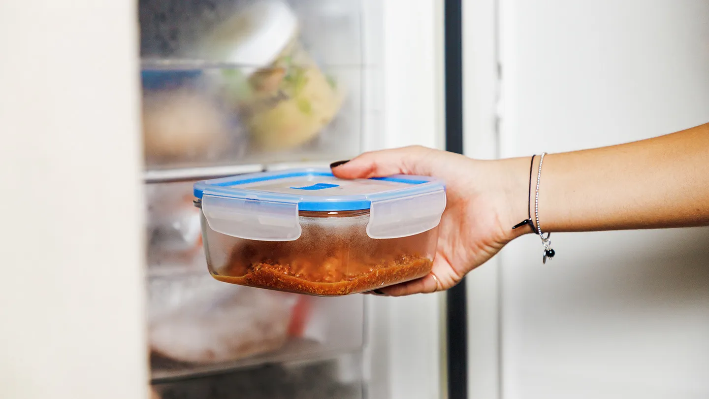 hand putting away a leftover meal in plastic container into a refridgerator