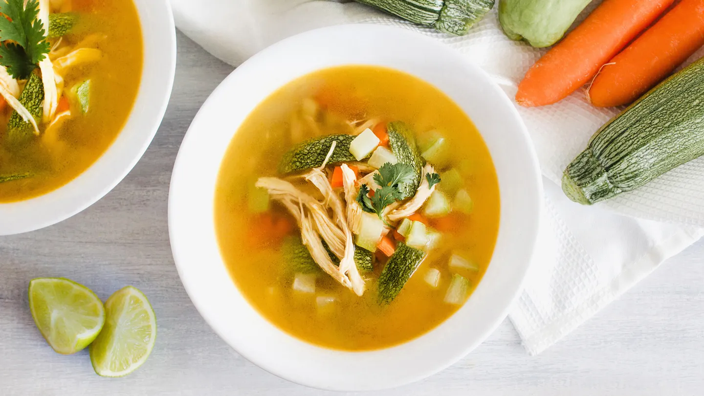 Bowl of chicken soup surrounded by vegetable ingredients