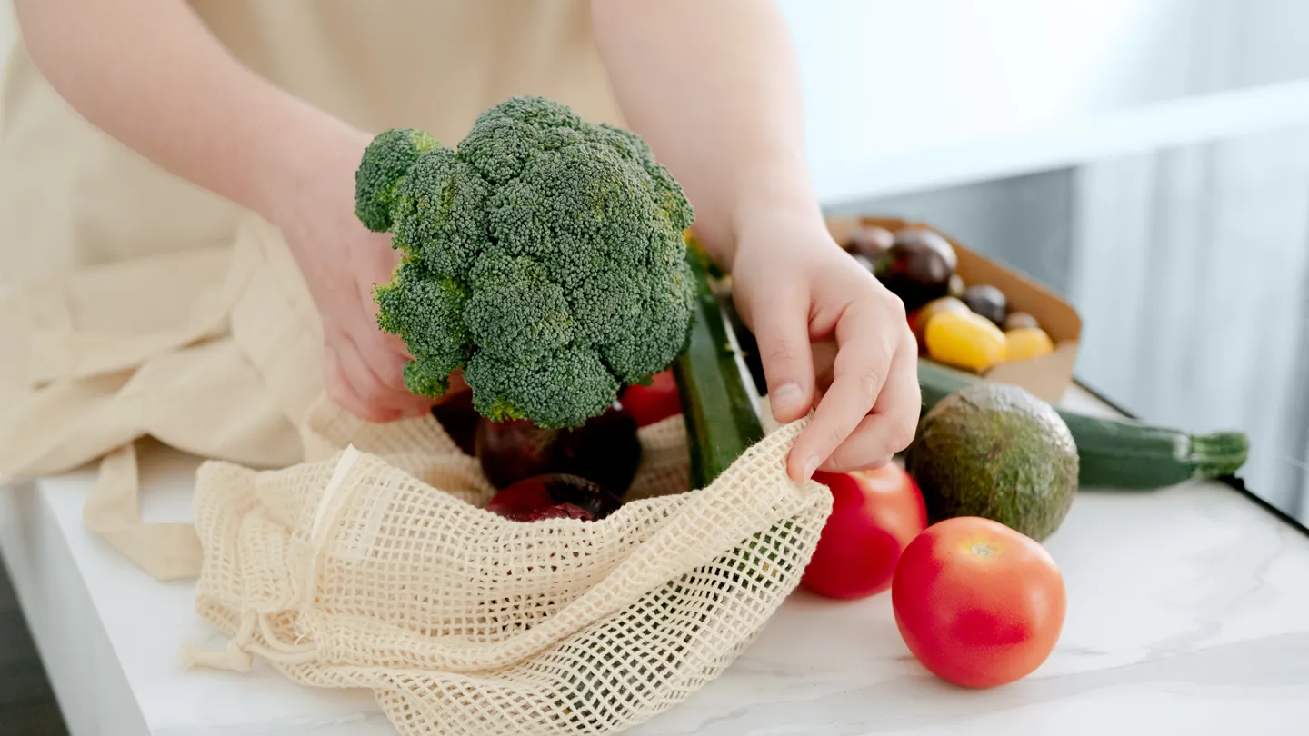 woman unpacking vegetables like broccoli and tomatoes from shopping bag in her kitchen