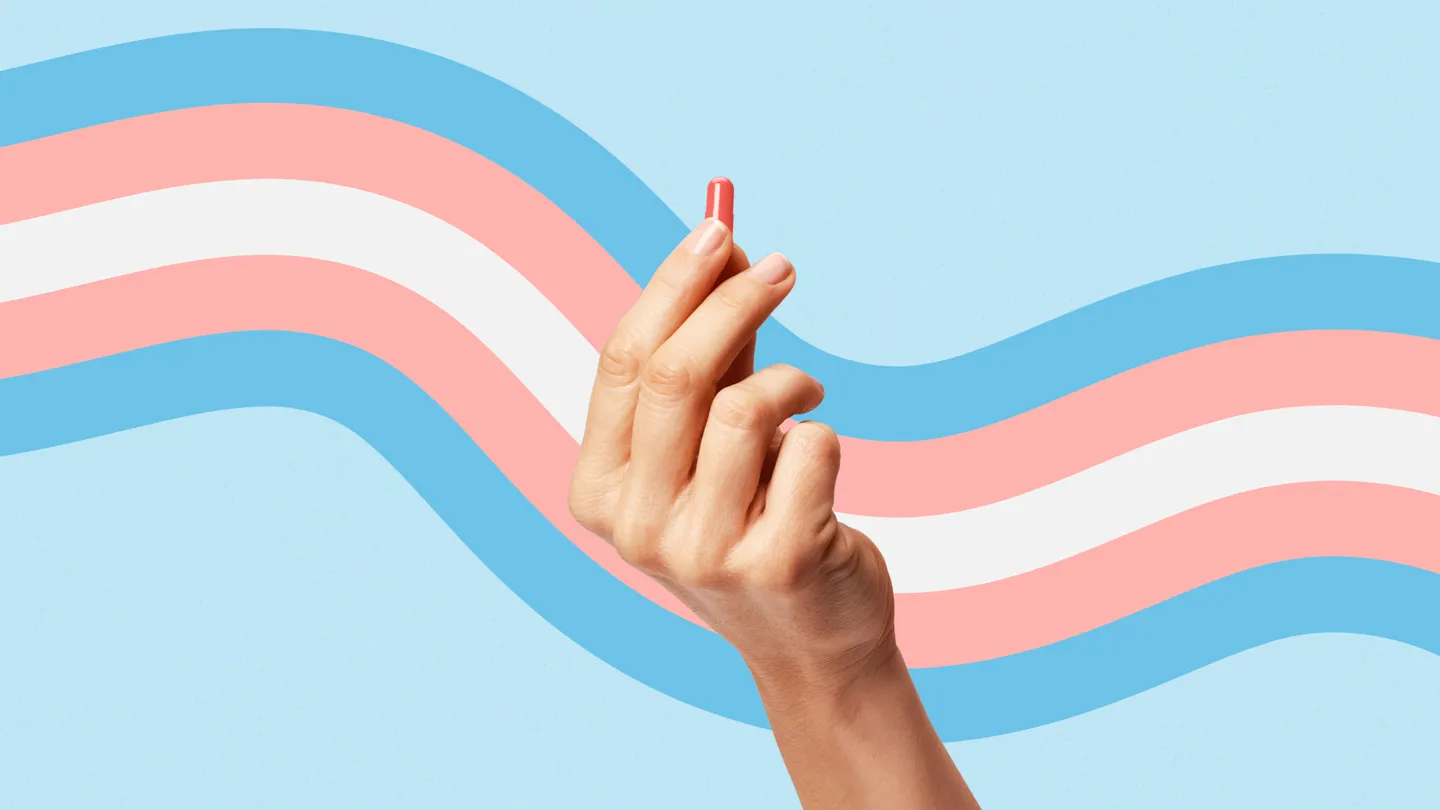 hand holding a pill in front of transgender flag colors