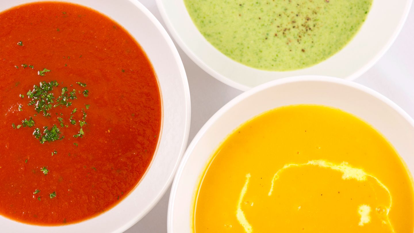Three types of soups in white bowls, tomato, squash, peas