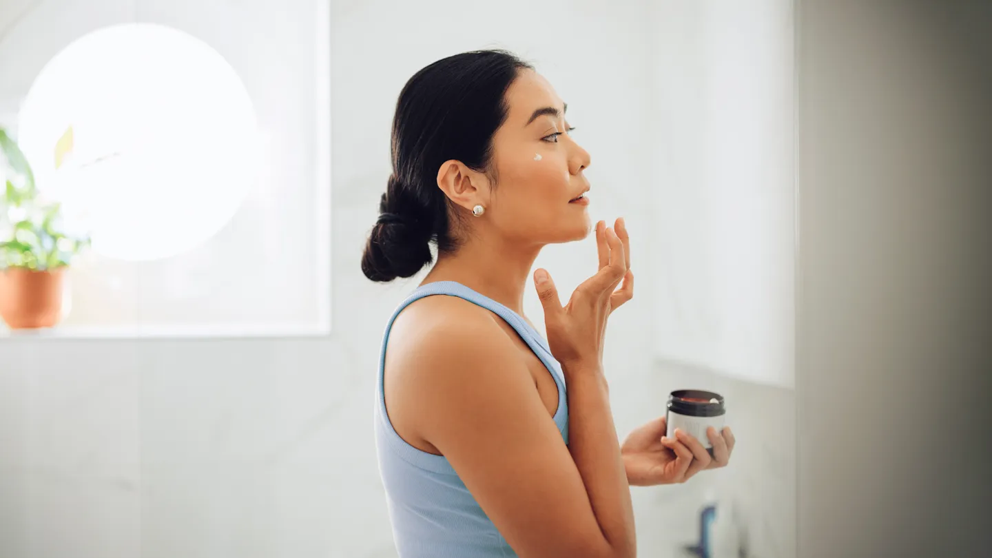 asian woman applying cream to face in bathroom