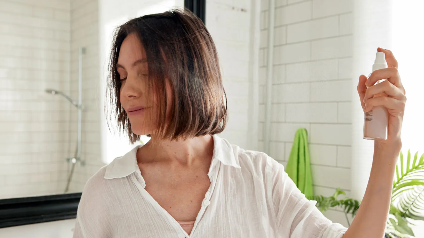 woman applying heat protectant spray to hair
