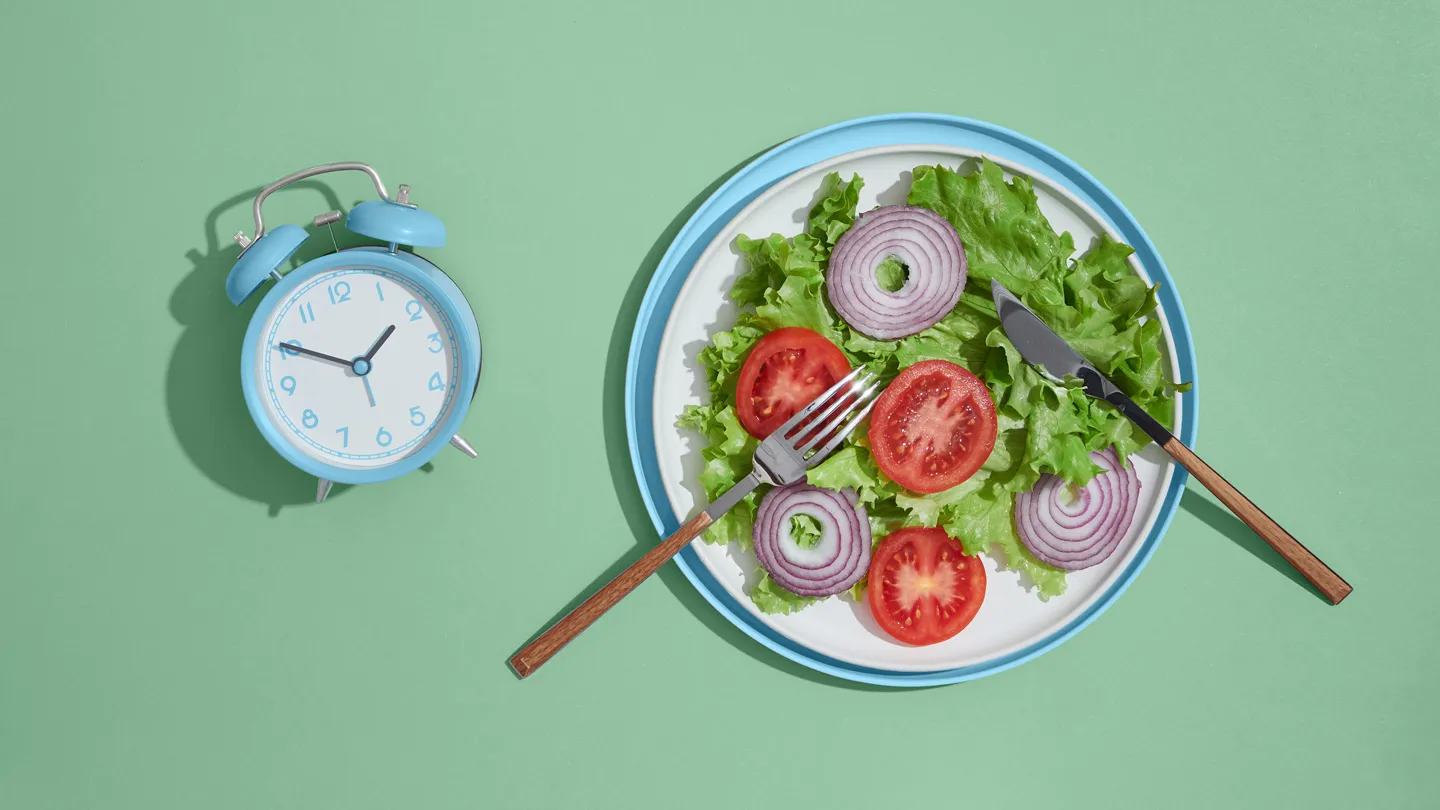 plate of salad with an alarm clock next to it indicating timed meals due to intermittent fasting
