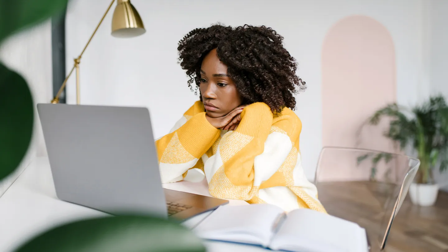 stressed young Black woman at work on a laptop in modern office