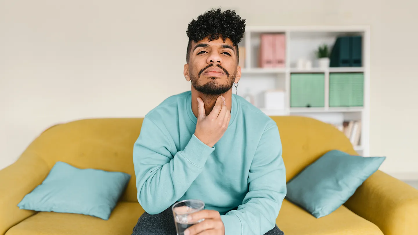 man with itchy throat sitting on couch with a glass of water
