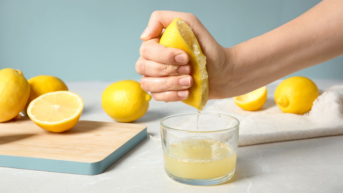 a hand squeezing a lemon to collect lemon juice