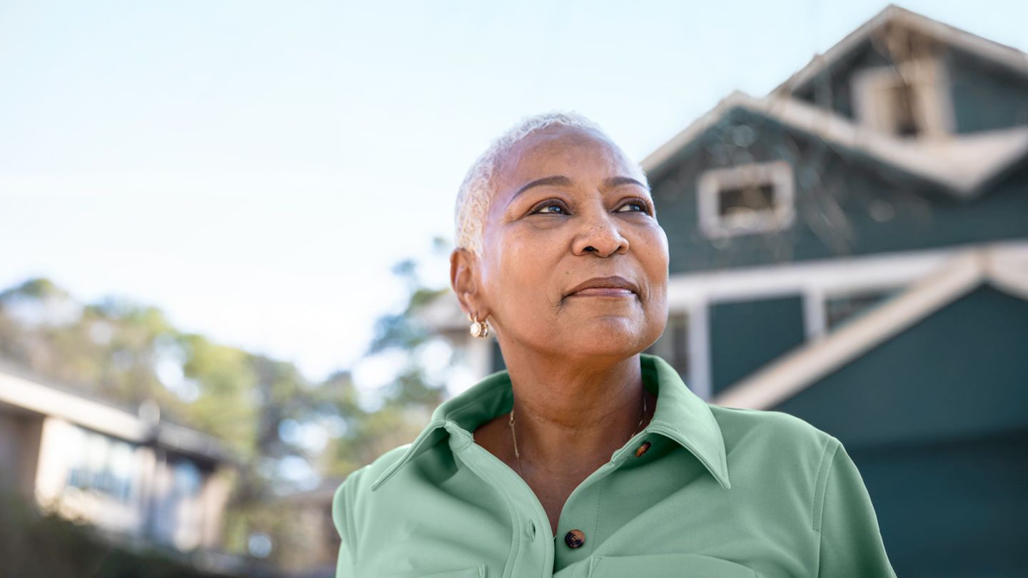 mature Black woman looking into the distance standing in front of her home