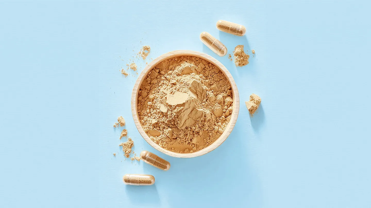 maca root supplement capsules and maca powder in wooden bowl on blue background