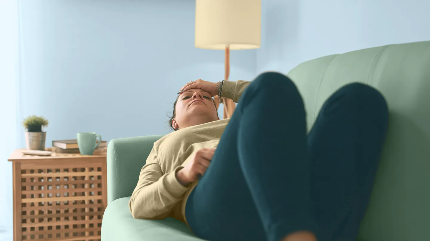 woman lying on couch with head and stomach aches