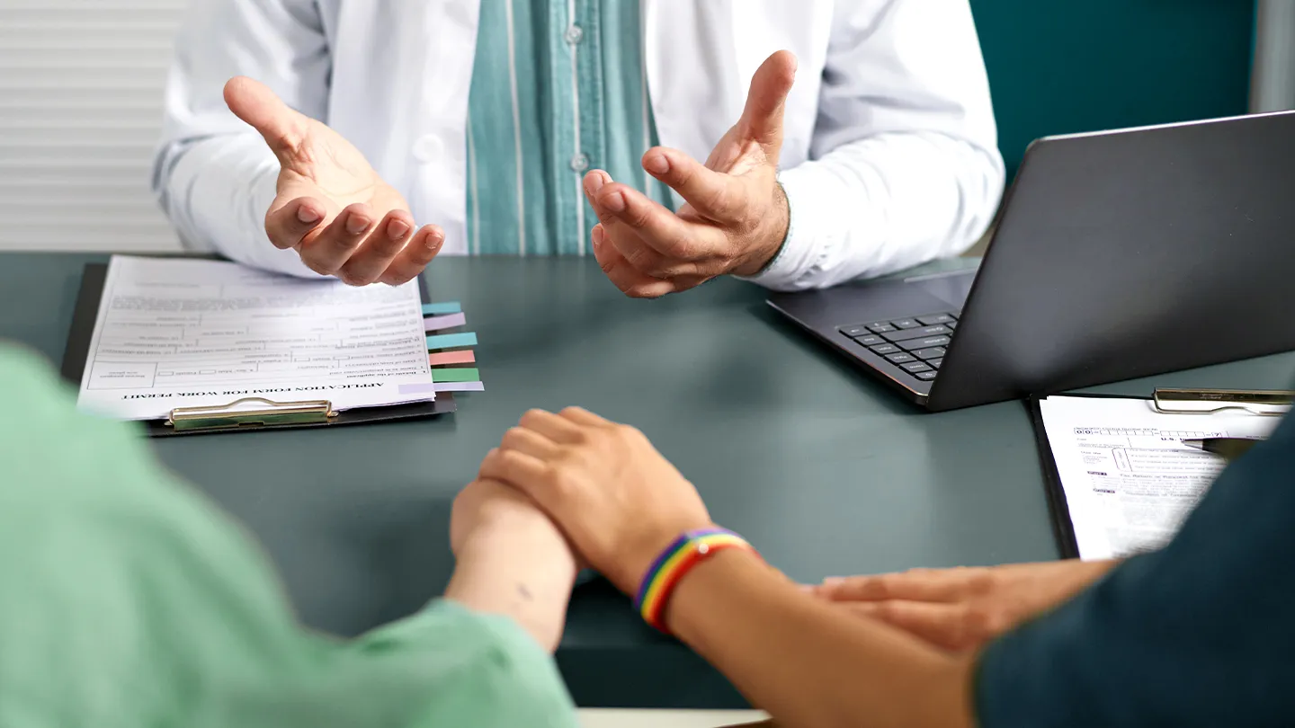 lgbtq couple holding hands while doctor talks