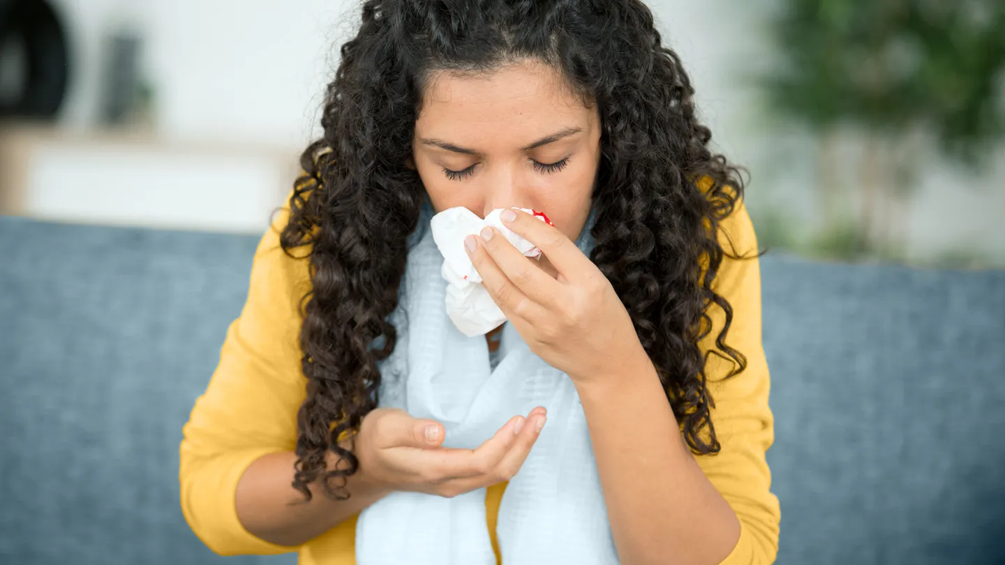 young woman sitting on couch trying to stop a nosebleed nose bleed