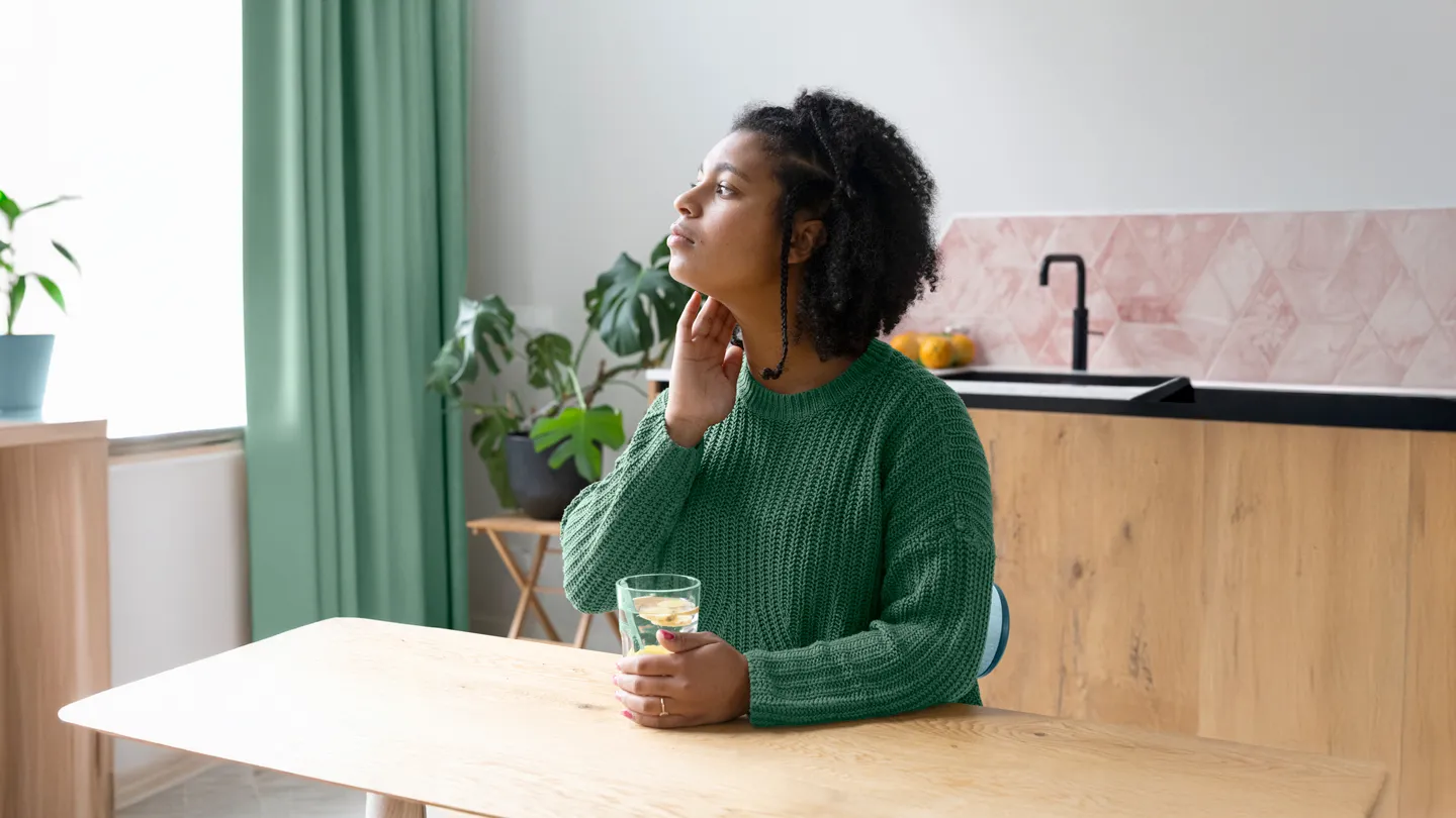 woman holding her jaw with nausea at kitchen table holding a glass of lemon water