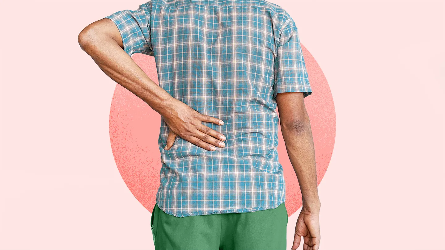 man in blue shirt and green shorts holding hand on lower back lower back pain